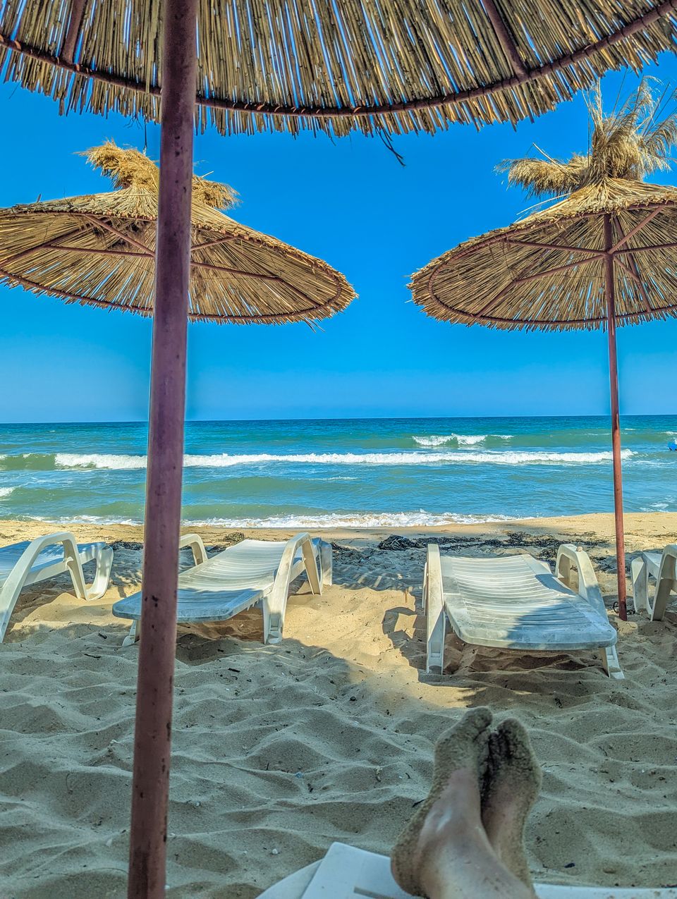 Sonnenliegen unter Strohschirmen am Strand von Obzor mit Blick aufs Meer